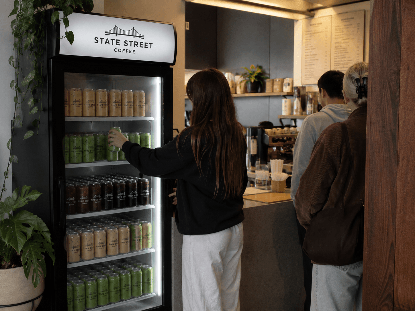 A customer grabbing a canned drink from a cafe cooler stocked with cans